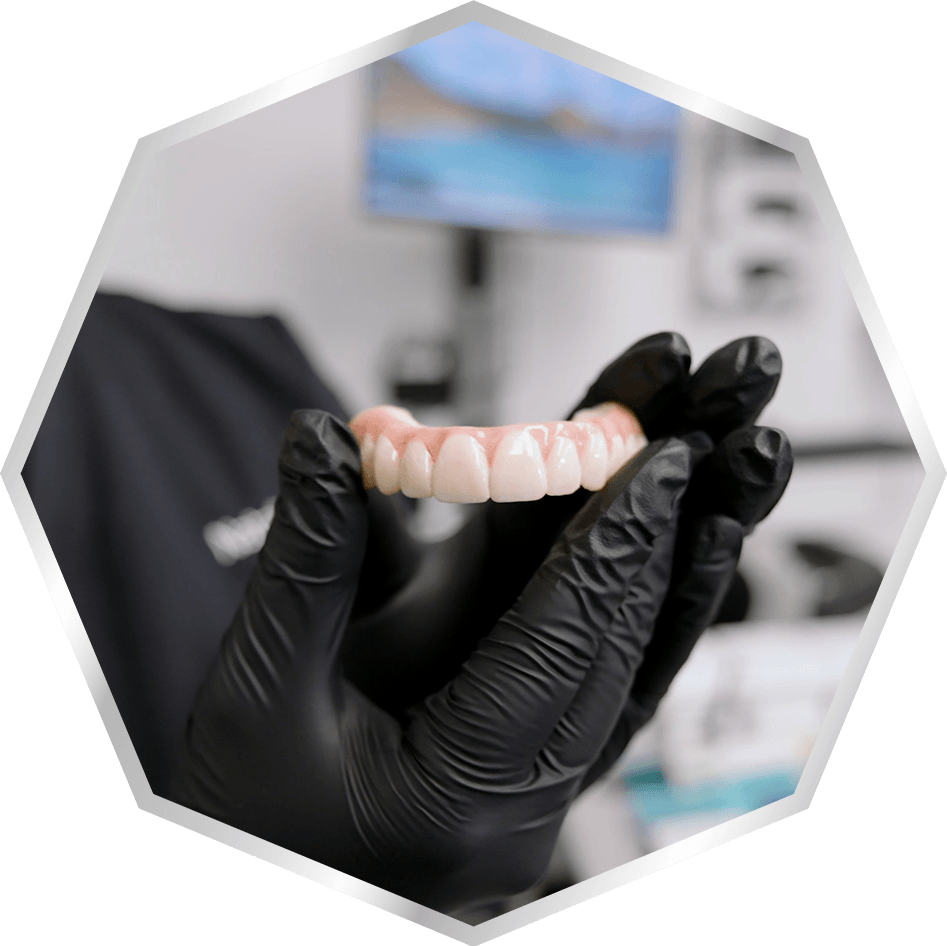 Close-up of a dental team member wearing black gloves and holding a full-arch dental prosthesis.